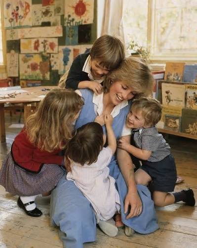 Princess Diana kneeling on the floor, embraced by a group of young children